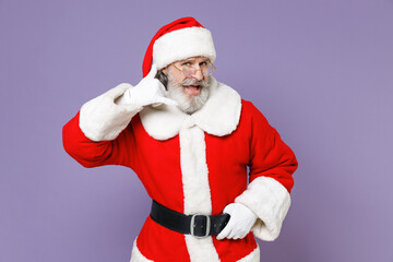 Fototapeta na wymiar Funny Santa Claus man in Christmas hat red suit coat gloves glasses doing phone gesture like says call me back isolated on violet background studio. Happy New Year celebration merry holiday concept.