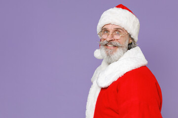 Side view of smiling elderly gray-haired Santa Claus man in Christmas hat red suit coat glasses looking camera isolated on violet background studio. Happy New Year celebration merry holiday concept.