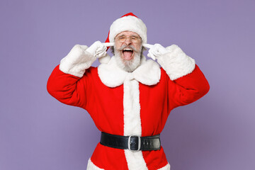 Frustrated Santa Claus man in Christmas hat red coat glasses covering ears with fingers keeping eyes closed screaming isolated on violet background. Happy New Year celebration merry holiday concept.