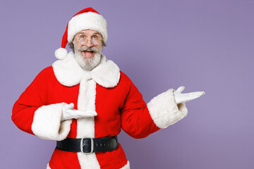 Fototapeta na wymiar Excited elderly gray-haired Santa Claus man in Christmas hat red suit coat gloves glasses pointing hands aside isolated on violet background studio. Happy New Year celebration merry holiday concept.