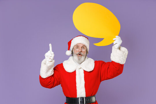 Amazed Santa Claus man in Christmas hat red coat hold yellow blank empty Say cloud point index finger up with new idea isolated on violet background. Happy New Year celebration merry holiday concept.