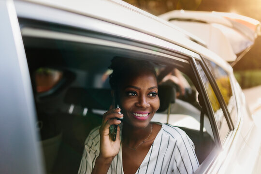 Cheerful black woman speaking on smartphone while riding in car