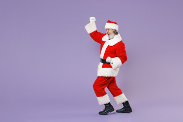 Full length side view portrait Santa Claus man in Christmas hat red suit coat white gloves glasses doing winner gesture isolated on violet background. Happy New Year celebration merry holiday concept.