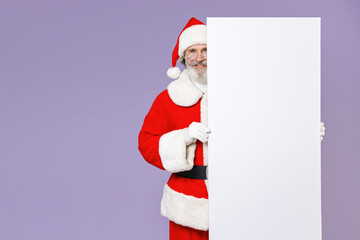 Smiling funny Santa Claus man in Christmas hat red coat suit gloves glasses hold big white empty blank billboard isolated on violet background studio. Happy New Year celebration merry holiday concept.
