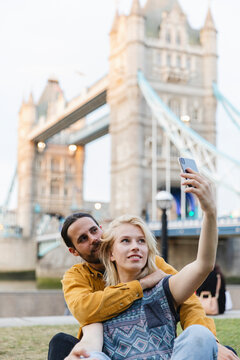 Sitting couple taking a selfie with the Tower Bridge in the background