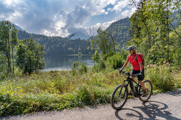 nice senior woman riding her electric mountain bike above the Freiberg Lake and a big ski flying hill in the Allgau Alps near Oberstdorf, Bavaria, Germany
