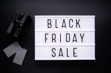 Black Friday Sale words on lightbox with black giftbox and price tags top view flat lay on black background