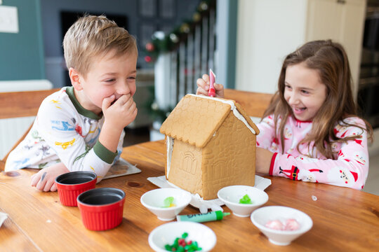 Brother and sister decorating a gingerbread house for the holidays