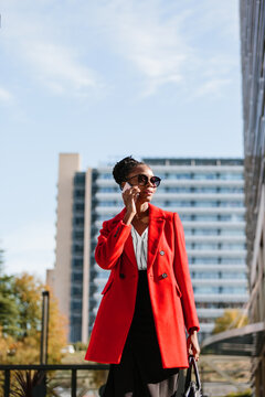 Enthusiastic black woman in red coat discussing on smartphone in downtown