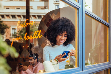 Smiling African American woman using smartphone in cafe