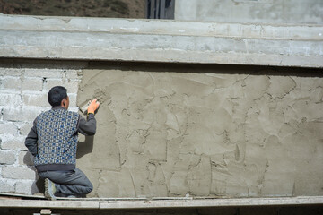 Chinese worker adding a layer of cement to a wall of bricks