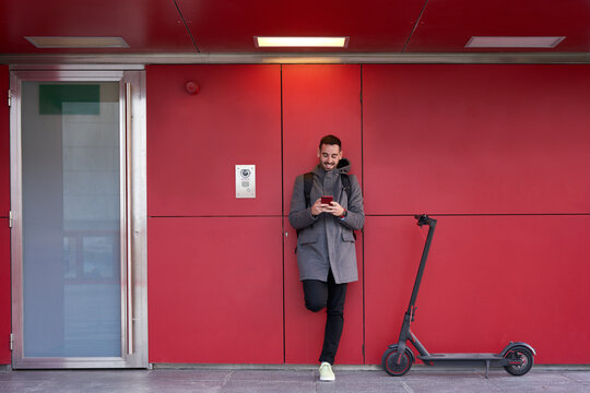 Cheerful Man Using Smartphone Near Electric Scooter