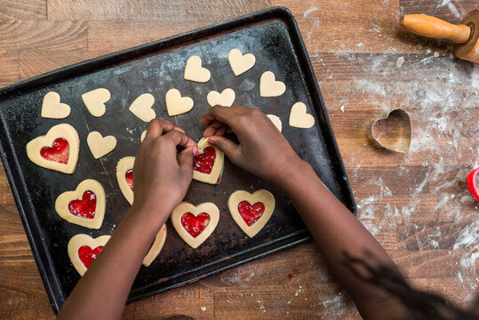 Black girl's hands placing a heart shaped cookie in a baking tra