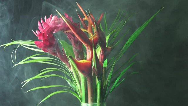 Bouquet of tropical exotic flowers in the forest rain fog. Close-up shot of Heliconia rostrata floral arrangement from rainforest garden. Leaf background with Bird of paradise and Lobster Claw fern.
