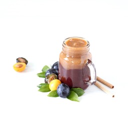 Smoothies combined from black and yellow plums in a glass jar with bamboo straws on a white...