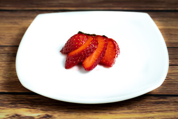 Aerial view of a strawberries cut into slices on white plate and rustic background