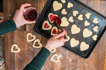 Woman's hands putting jam on Valentine's Day cookies