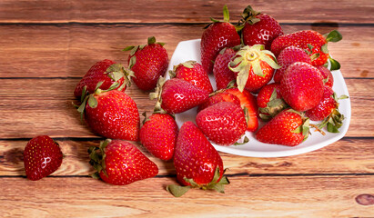 Strawberries on a white square plate on a wooden table in a rustic setting