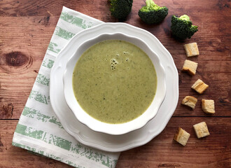 Broccoli cream soup with croutons and herbs on stone background.