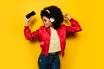 Beautiful afro woman listening to music with white headphones and cellphone