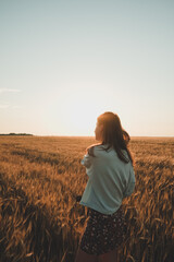 Fototapeta premium Amazing Girl on the wheat field at sunset. Nature landscape with dramatic clouds sunset sky. Summer background. Rear view, contour light. Travel concept