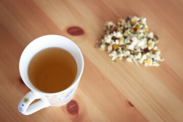 Top view of a cup of chamomile tea and dried flowers of chamomile on the wooden table.