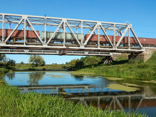 a freight train travels on a metal railway bridge, reflections in the river 