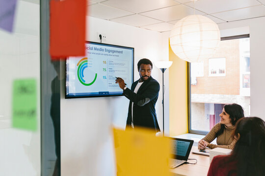 Black man presenting report on TV to coworkers in office