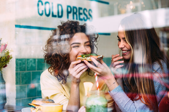 Cheerful woman feeding friend in cafe