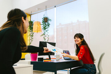 Smiling women passing paper to each other