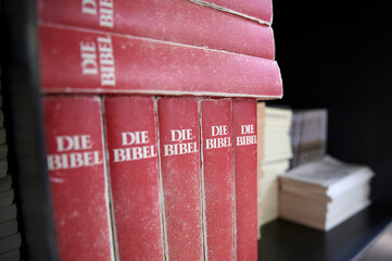 Bibeln in einem roten Einband stehen nebeneinander in einem Bücherregal einer katholischen Kirche
