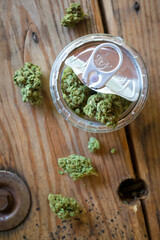 Cannabis in an open plastic jar with a pop-top tin lid - overhead top view