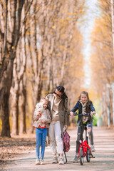 Little girls with mom outdoors in park at autumn day