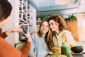 Female friends taking pictures with smartphone in cafe