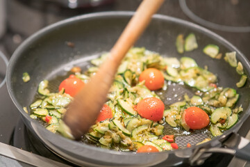 Stirring vegetables, zucchini, onion and tomato, in a pan. Selective focus