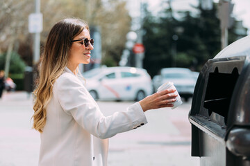 Woman throwing a cardboard glass into a recycling bin
