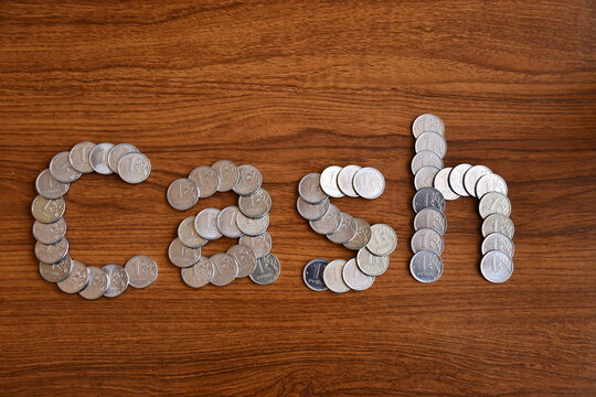 The word Cash is laid out on a wooden brown surface of Russian modern coins with a face value of one ruble.