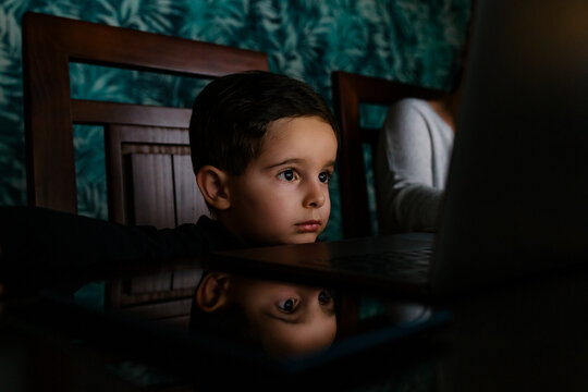 Mother working at home while her bored son look at laptop screen