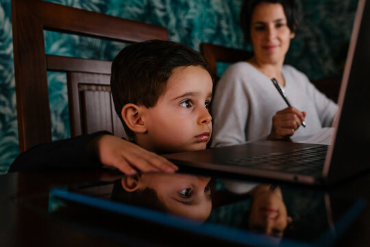 Mother working at home while her bored son look at laptop screen