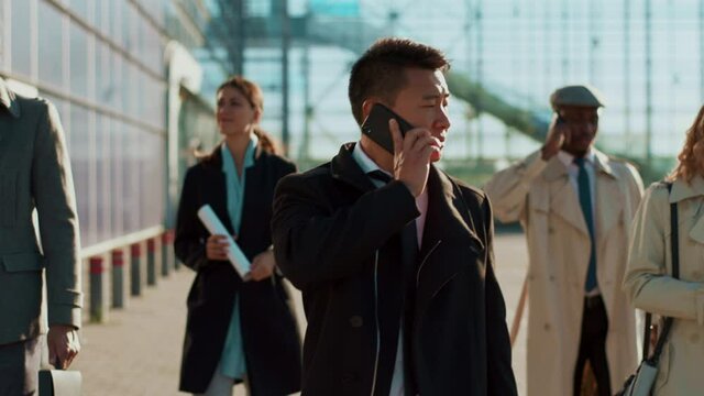 Career people. Busy confident asian man talking mobile converation with clients while walking along business district. Corporate people. Business team.