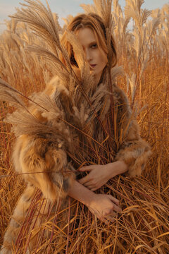 beautiful red-haired model in a fur coat stands, hugging a sheaf of tall yellow grass