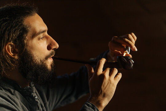 dark-haired bearded guy lights a pipe