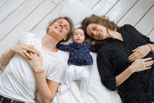 young parents and their little daughter lie on the mattress and look up
