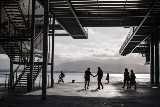 People in silhouette passing under the awning of a contemporary seafront building