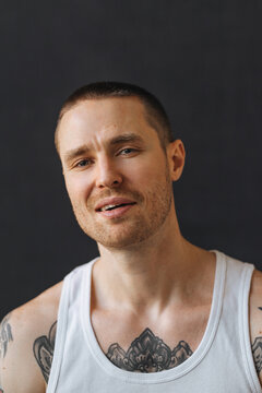 portrait of a smiling tattooed guy in a white t-shirt on a dark background