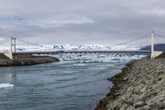 Icebergs float towards the open arctic sea, passing under a suspended bridge in jokulsarlon in iceland - Powered by Adobe
