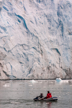 A person is rowing a dinghy towards the wall of a huge glacier
