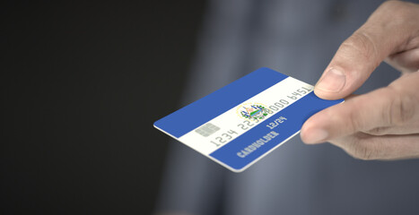 Man gives credit card with flag of El Salvador. Fictional numbers