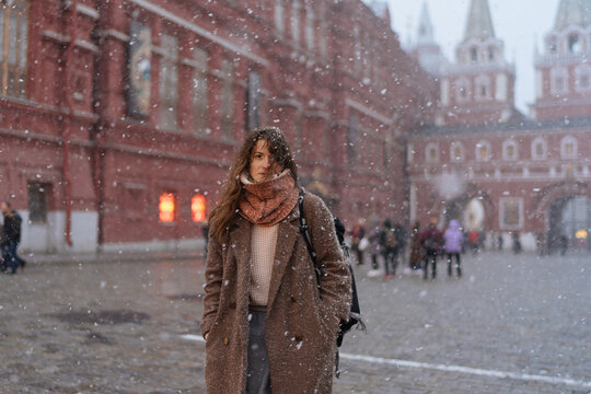 woman in a brown coat walks along the red square in Moscow during a snowfall