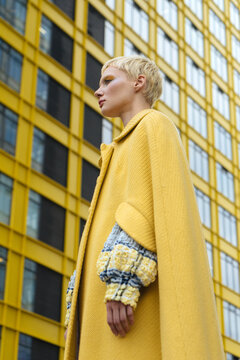 short-haired model in a yellow coat on a background of a yellow building